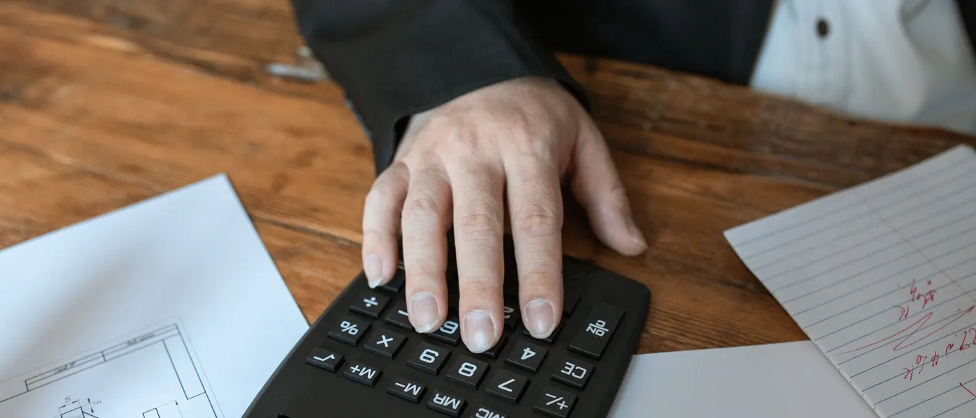 Handen die cijfers nakijken met een rekenmachine aan tafel